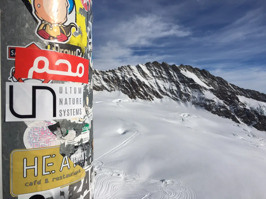 A UNS sticker on a post above a snow-covered glacier and mountain ridge